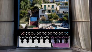 Vista a través de una ventana abierta con marco negro decorativo, mostrando una zona residencial con edificios de varios pisos, una palmera y un cielo azul despejado.