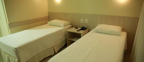 Habitación de hotel con dos camas individuales, cada una con almohada y mesita de noche con teléfono.
