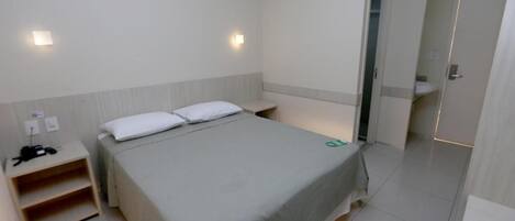 Una habitación de hotel con una cama, mesita de noche y un armario.