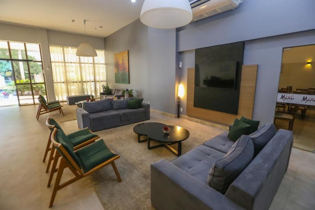 A modern living room with a grey sofa, green armchairs, a coffee table, and a large window with curtains.