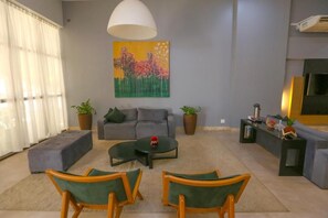 Olohuoneessa on harmaa sohva, sohvapöytä ja kaksi nojatuolia. Seinällä on taulu ja lattialla ruukkukasvi.