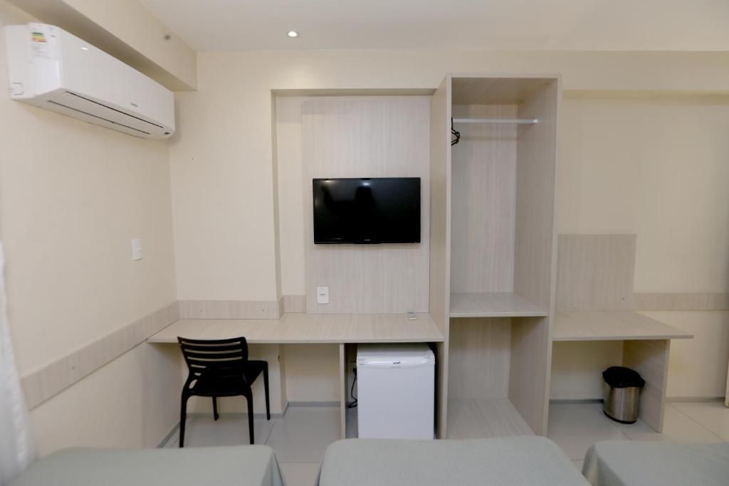 A compact room with a bed, a desk, a chair, a TV, and a mini-fridge.
