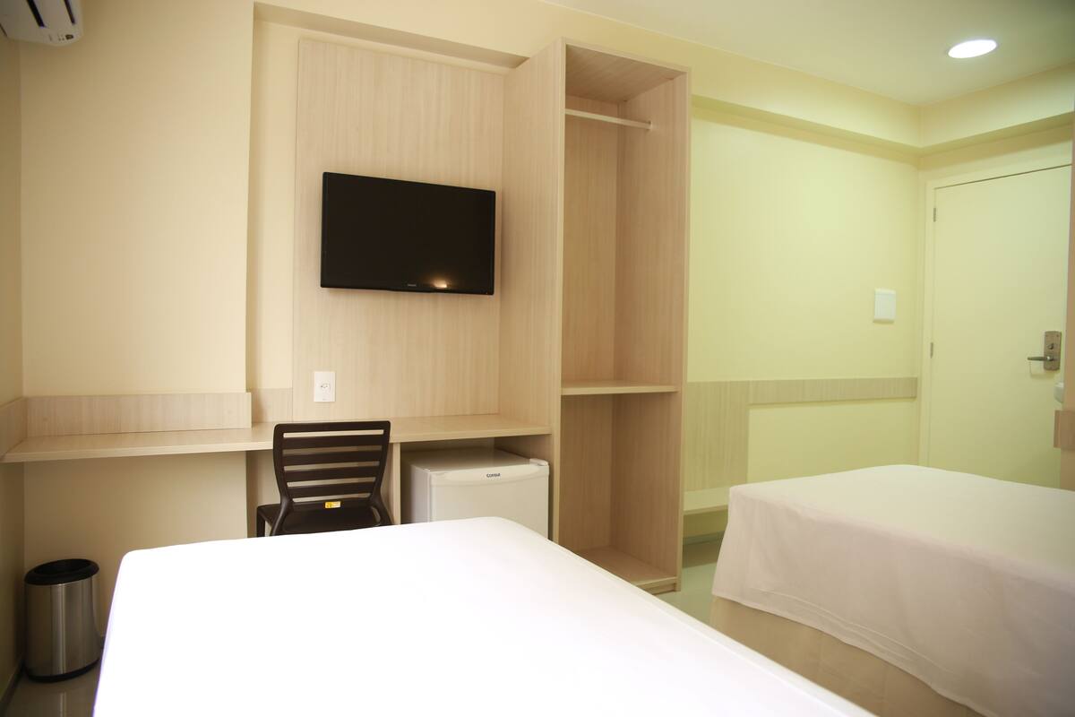Una habitación de hotel con cama, escritorio, silla, televisión y armario.