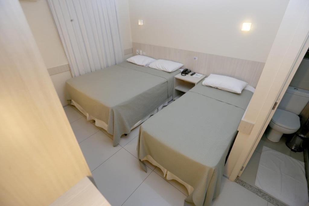 Habitación de hotel con dos camas individuales, una mesita de noche con teléfono, y baño con inodoro y ducha.