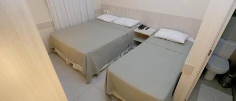 Habitación de hotel con dos camas individuales, una mesita de noche con teléfono, y baño con inodoro y ducha.