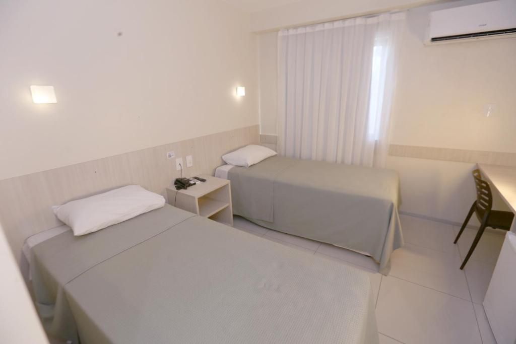 Une chambre d’hôtel avec deux lits simples, une petite table de chevet avec une lampe, une chaise et un appareil de climatisation.