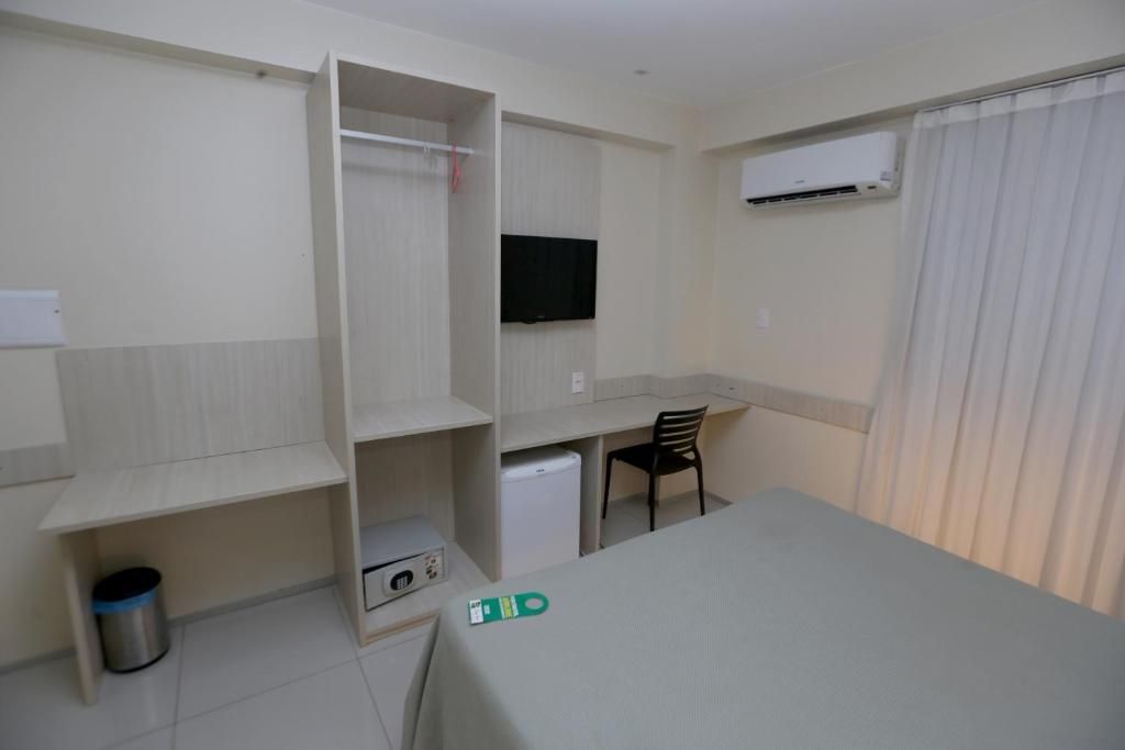 Een kleine hotelkamer met een bureau, stoel, kledingkast en een televisie.