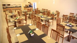A spacious dining area with multiple tables and chairs, a kitchen in the background, and a clean, well-lit environment. - Stay Inn Hotel (Imperatriz)