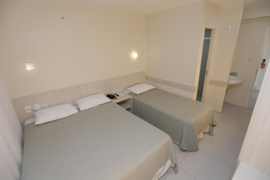 Una habitación de hotel con dos camas, una mesita de noche, una lámpara y un baño con lavamanos.