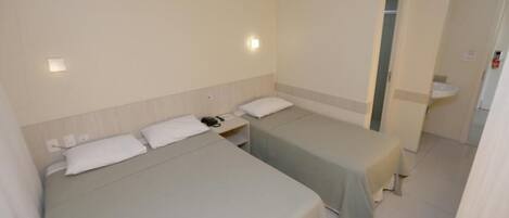 Una habitación de hotel con dos camas, una mesita de noche, una lámpara y un baño con lavamanos.