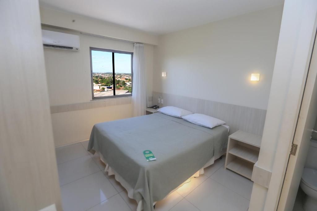 Une chambre d’hôtel avec un lit, une fenêtre donnant sur un paysage agréable, une table de chevet et un climatiseur fixé au mur.