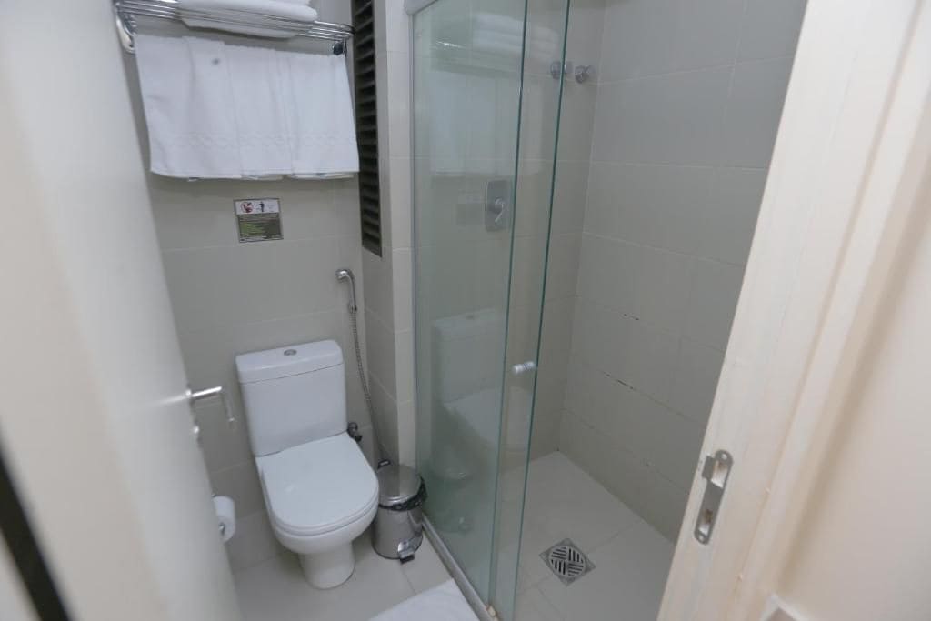 Een kleine badkamer met een toilet, een douche met glazen wand en een handdoekhouder.
