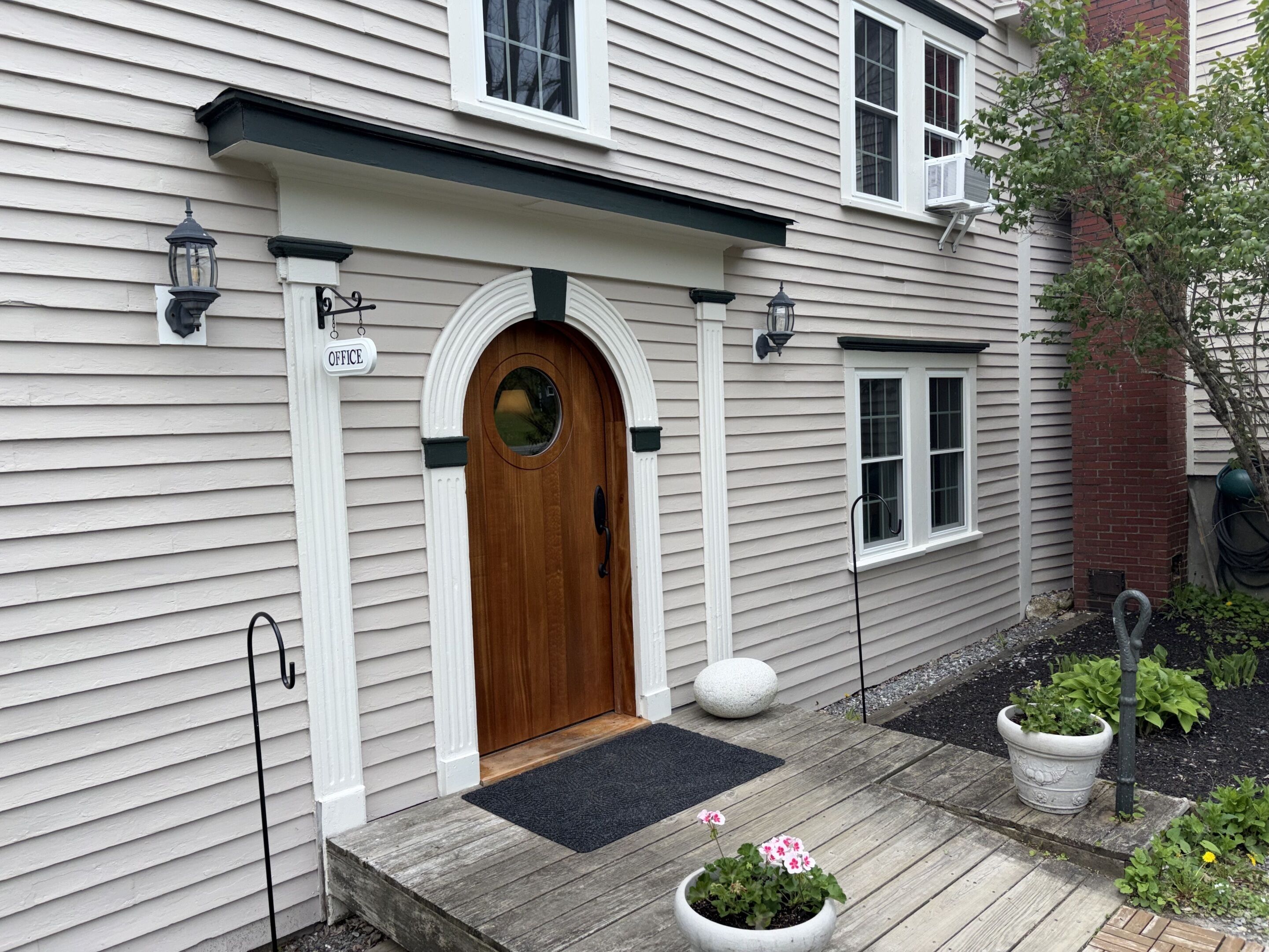 A house with a wooden front door, a small porch, and a sign indicating an office.