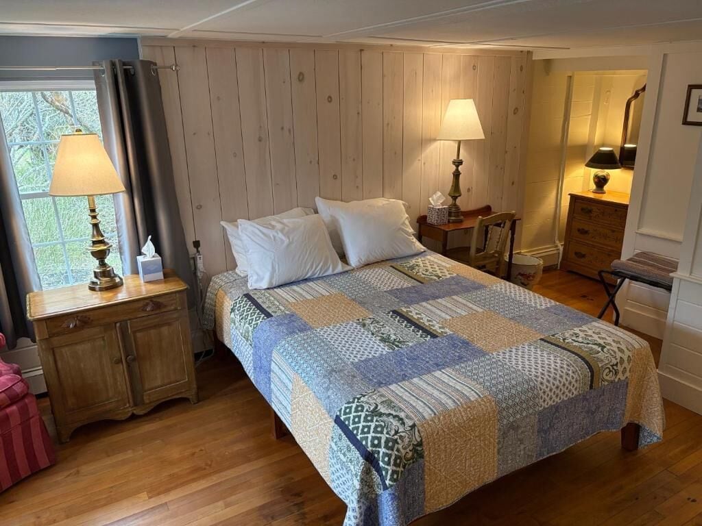 Un dormitorio con una cama grande, dos mesitas de noche con lámparas, un aparador y una ventana con cortinas.