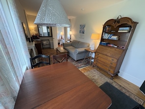 A dining area with a wooden table and chairs, a sofa, a lamp, and a bookshelf. - Hawks House Inn (Walpole)