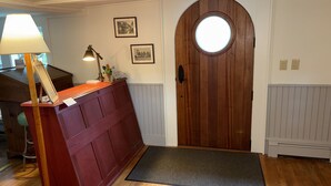 A wooden door with a circular window, a red bench with a lamp, and two framed pictures on the wall. - Hawks House Inn (Walpole)