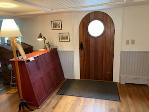 A wooden door with a circular window, a red bench with a lamp, and two framed pictures on the wall. - Hawks House Inn (Walpole)