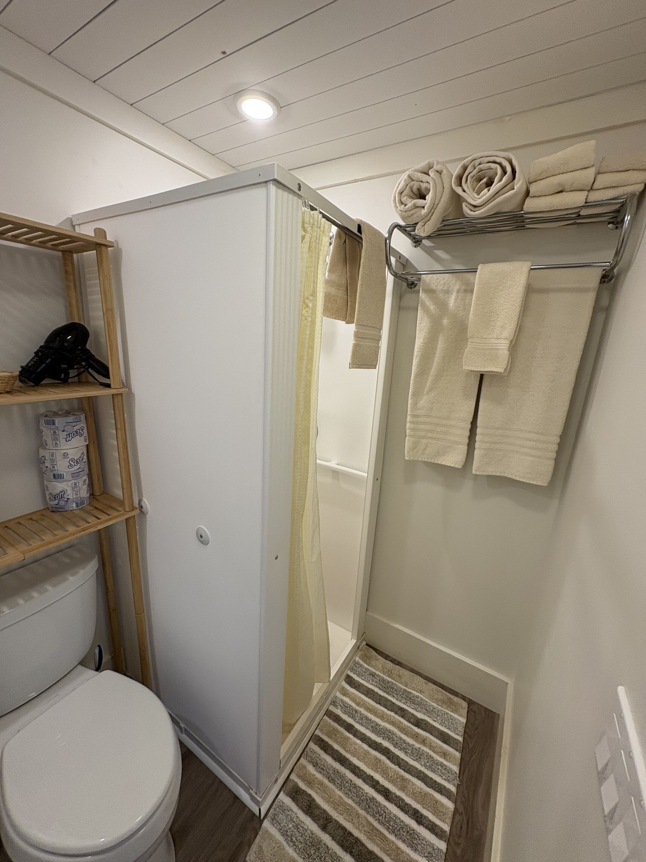 Un baño compacto con inodoro, zona de ducha y toallero con toallas ordenadamente dobladas.