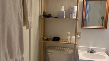 Un baño con inodoro, lavabo, espejo y estante con artículos de aseo.