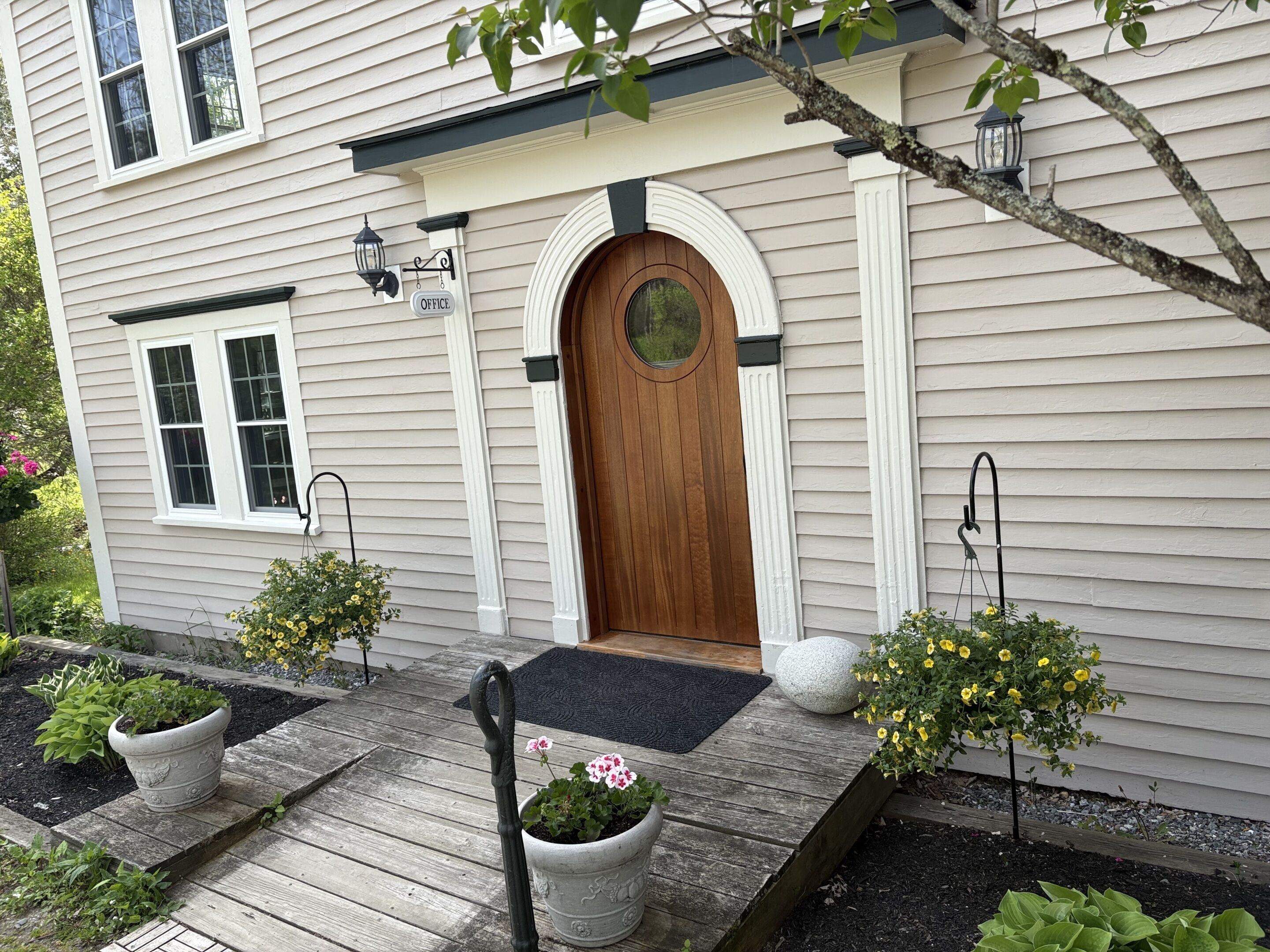 A house with a wooden front door, a porch with a black mat, and potted plants.