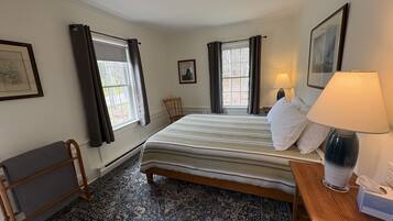 A bedroom with a bed, a chair, a radiator, a window with curtains, a lamp, and a picture on the wall.