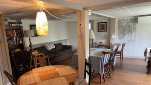 A dining area with a round wooden table, chairs, and placemats. There is a sofa and a bookshelf in the background. - Hawks House Inn (Walpole)