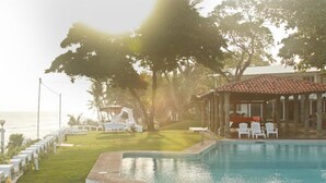 A pool area with a clear view of the ocean, surrounded by white lounge chairs and a covered seating area. - Quinta MonteCarlo (La Libertad)