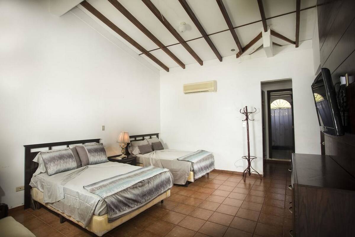 A bedroom with two beds, a TV, a coat rack, and a door leading to another room.