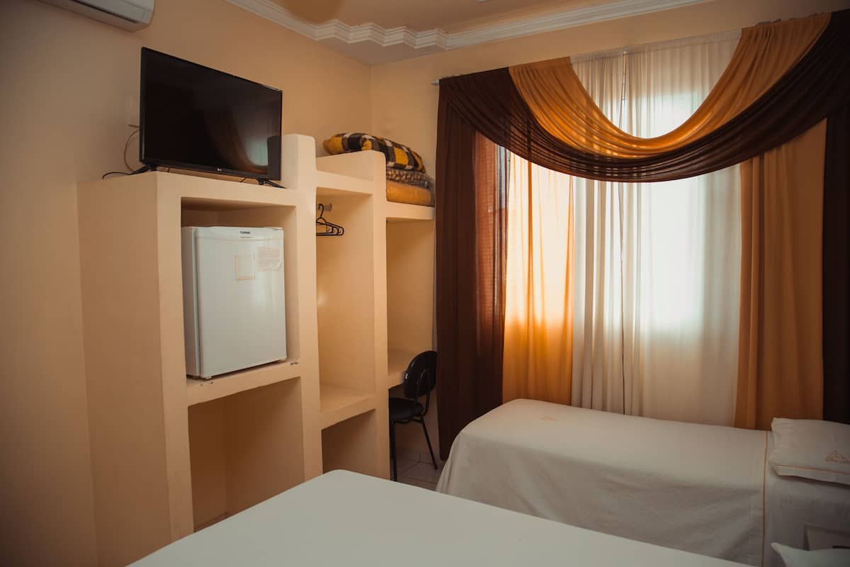 Quarto de hotel com duas camas, televisão, frigorífico e uma cadeira.