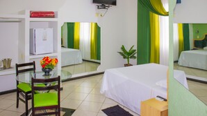Habitación de hotel con cama, escritorio con silla, una mesita con un florero, televisión y refrigerador.