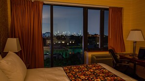 Habitación de hotel con un ventanal grande, una cama con colcha estampada, dos lámparas y un escritorio con silla.