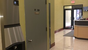 Una habitación de hotel con un mini bar, una puerta con la etiqueta 'RPZ ROOM' y un mostrador de recepción al fondo.