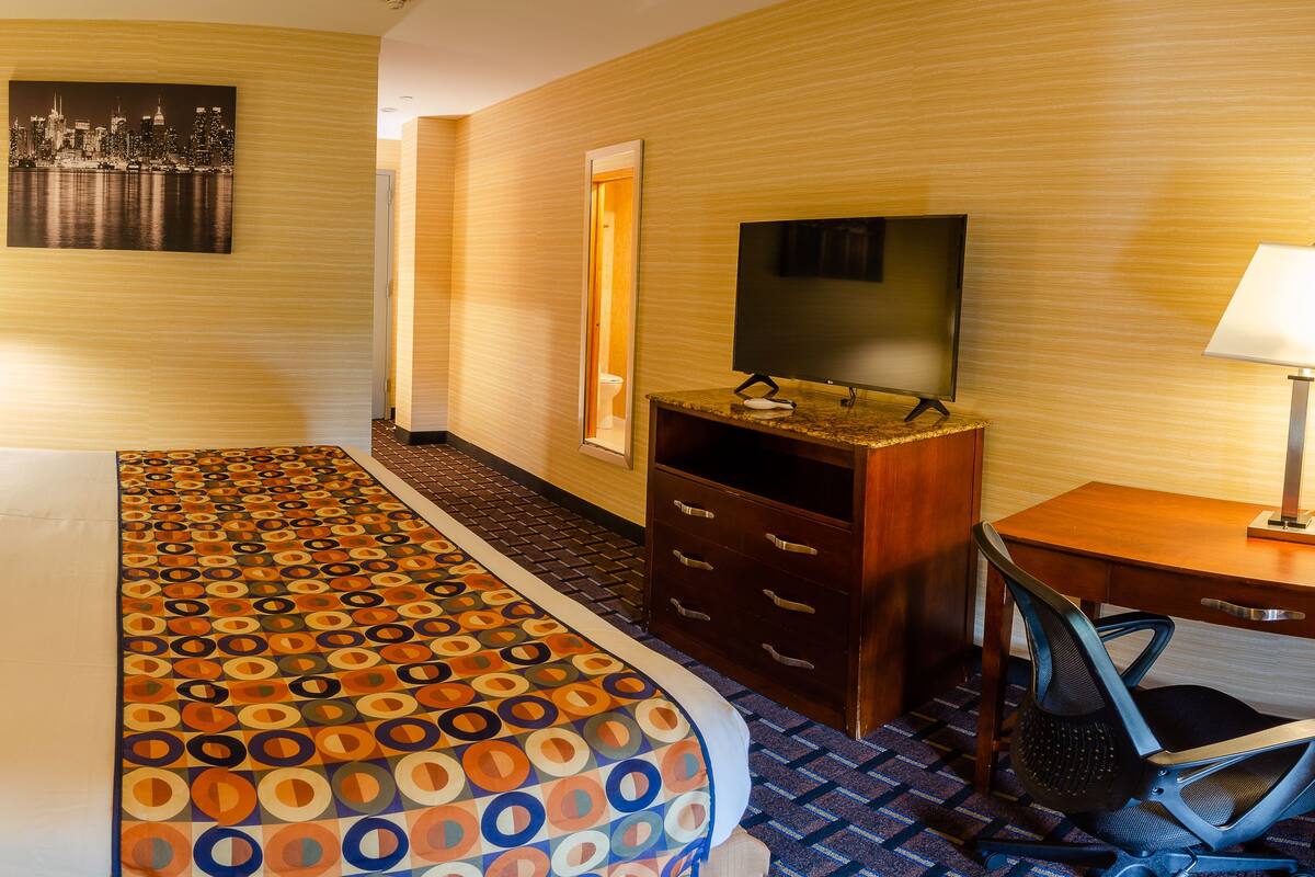 A hotel room with a bed, two bedside lamps, a television, a desk with a chair, and a patterned carpet.