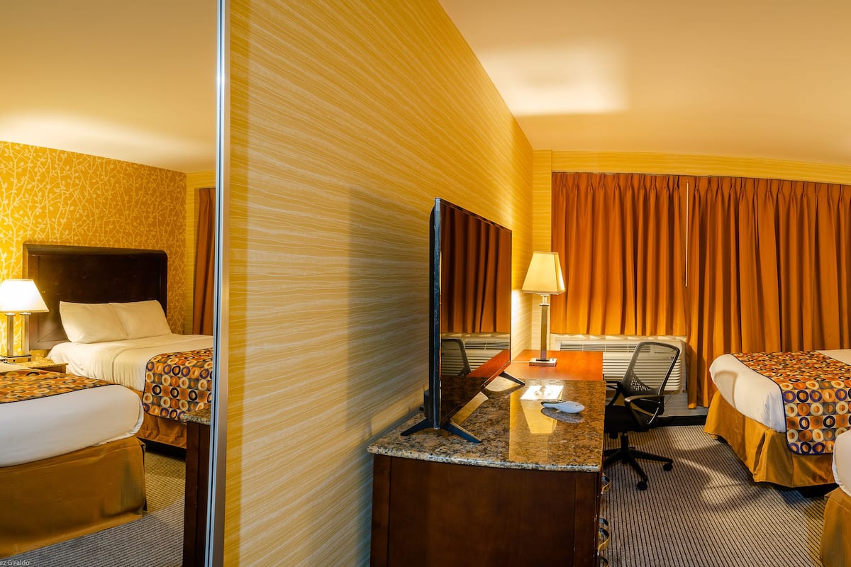 A hotel room with two beds, a desk, a chair, a mirror, and a window with curtains.