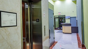 Un pasillo interior con un ascensor, un mostrador de recepción y un cartel de plan de evacuación contra incendios.