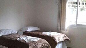 Ein Zimmer mit zwei Betten, einem fensterbelaubten Fenster und einer Wand-Klimaanlage.