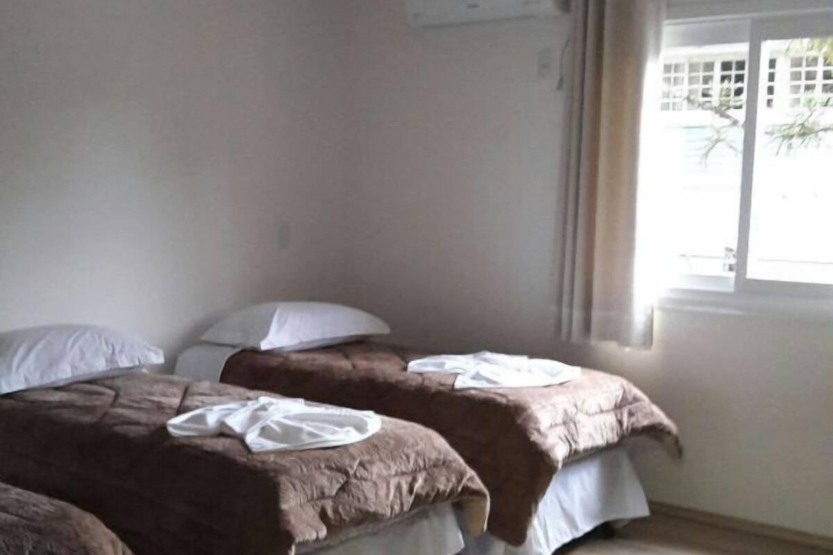 Una habitación con dos camas, una ventana con cortinas y un equipo de aire acondicionado en la pared.
