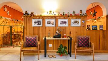 Una habitación acogedora con paredes de madera, dos sillones a cuadros, una mesita con lámpara y varios objetos decorativos, como fotografías enmarcadas y figuritas.