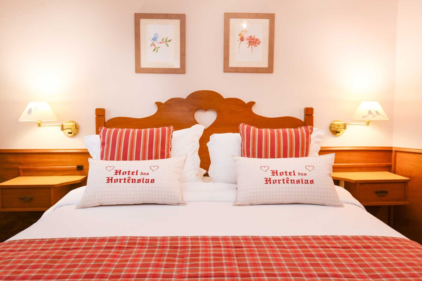 Une chambre d’hôtel avec une tête de lit en bois, deux tables de chevet avec des lampes et deux oreillers ornés de motifs brodés.