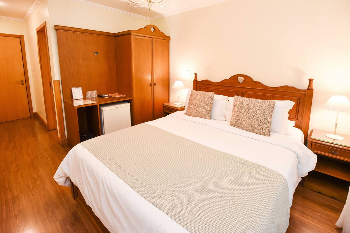 Una habitación de hotel con una cama grande, un armario de madera, mesitas de noche y un escritorio.