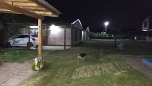 Un espace extérieur aménagé pour la nuit, avec une pelouse verdoyante, une pergola en bois et un bâtiment en briques.