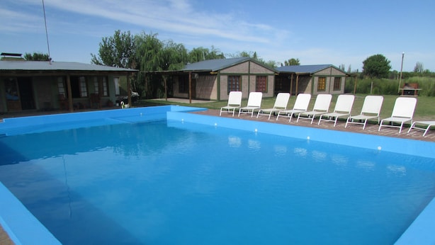 Une piscine rectangulaire aux parois bleues, bordée d’une allée en briques. Des chaises longues blanches sont alignées le long du bord de la piscine.