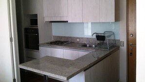 Una cocina con armarios blancos, un lavamanos de acero inoxidable, una estufa y un microondas.