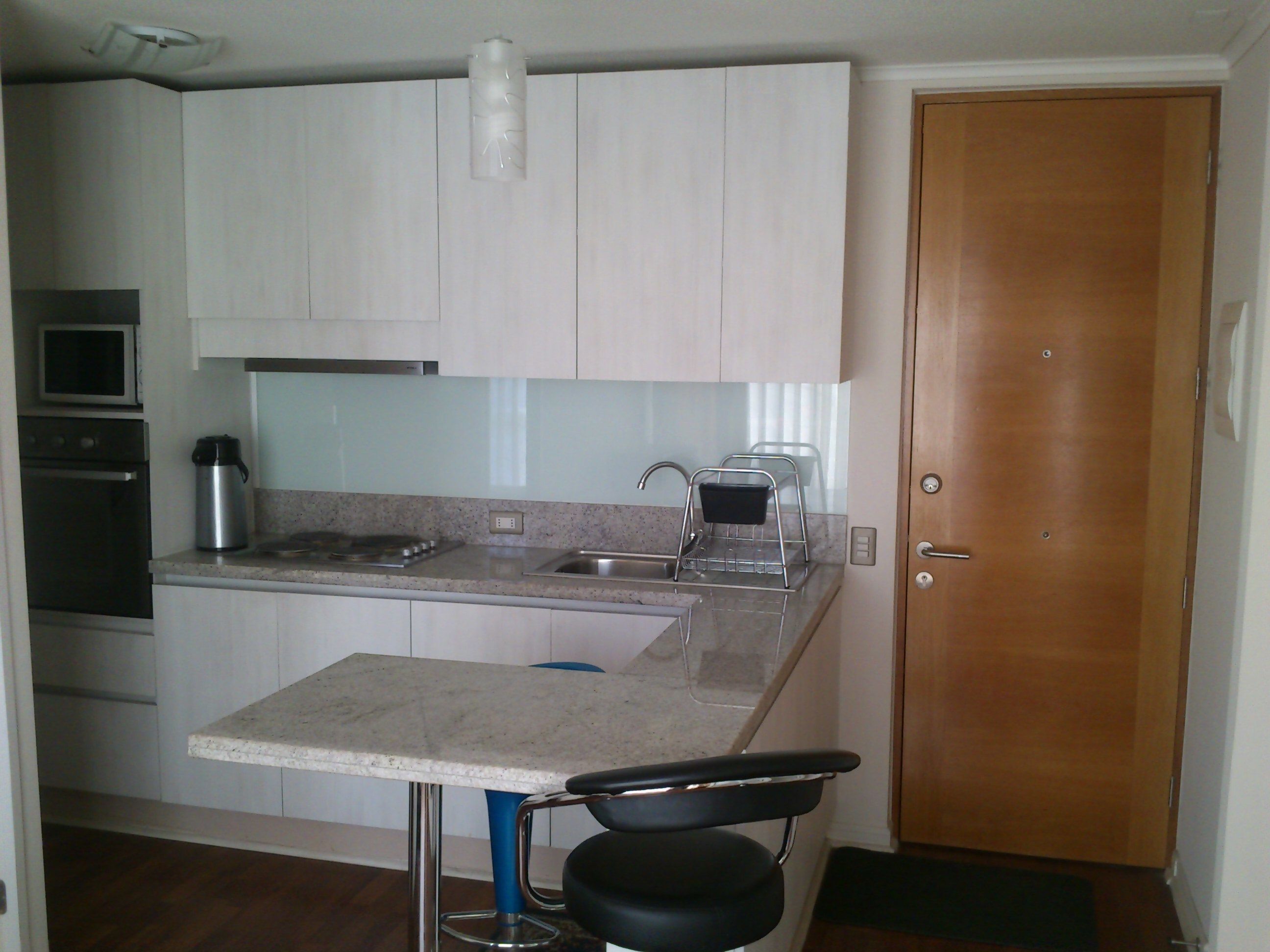 A compact kitchen with white cabinets, a stainless steel sink, a coffee maker, and a small bar stool.