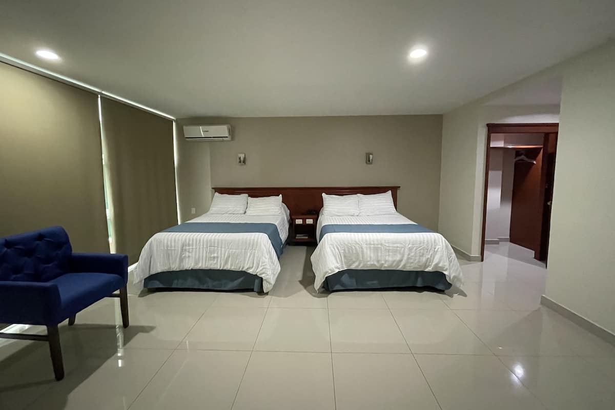 A hotel room with two beds, a blue chair, and a wooden wardrobe.