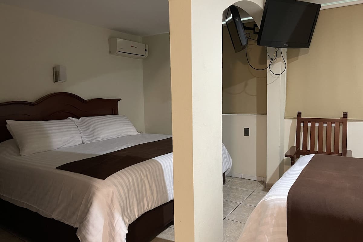 A hotel room with a bed, a television mounted on the wall, and an air conditioning unit.