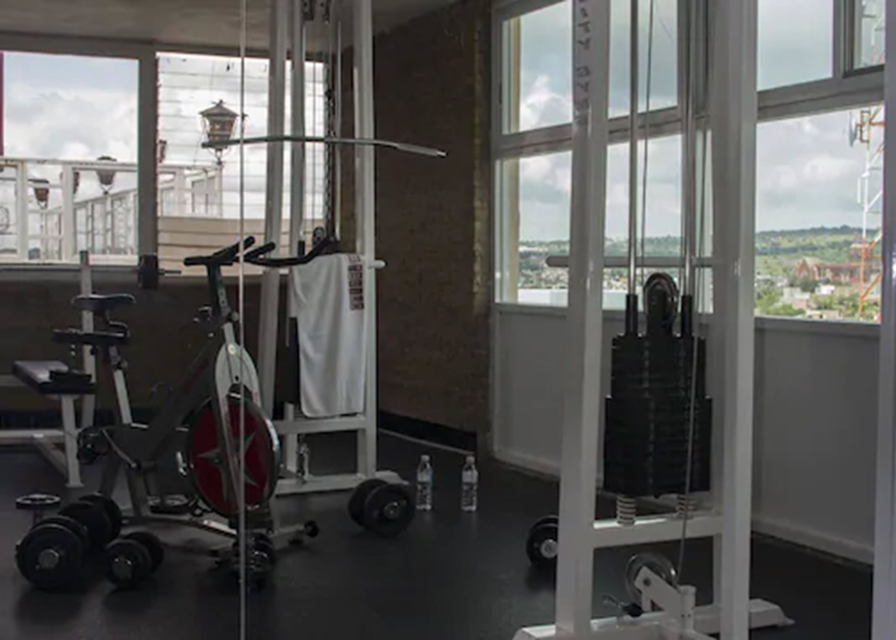 Un gimnasio con diferentes equipos de ejercicio, ventanas amplias y vistas al exterior.