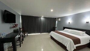 Una habitación de hotel con cama, escritorio, silla, televisión y ventana con cortinas.