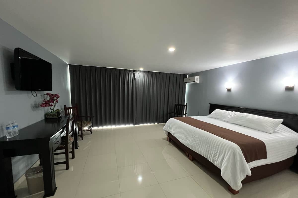 A hotel room with a bed, a desk, a chair, a TV, and a window with curtains.