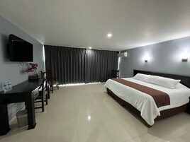 Quarto de hotel com cama, escrivaninha, cadeira, televisão e janela com cortinas.